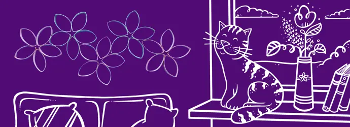 Cat on a windowsill beside flowers and books, with cardboard wall art flowers above a sofa in a cosy room scene.