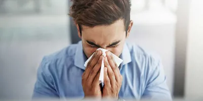 Young man sneezing and blowing his nose with a tissue