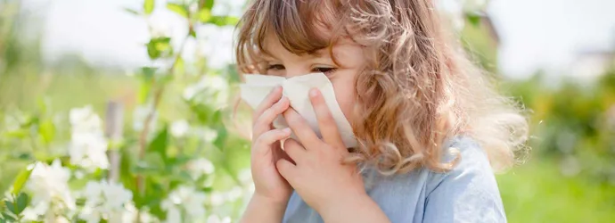 Little girl blowing her nose to relieve pollen allergy