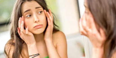 Teenager checking her swollen eyes from allergies in the mirror