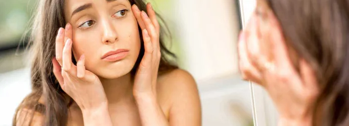 Teenager checking her swollen eyes from allergies in the mirror