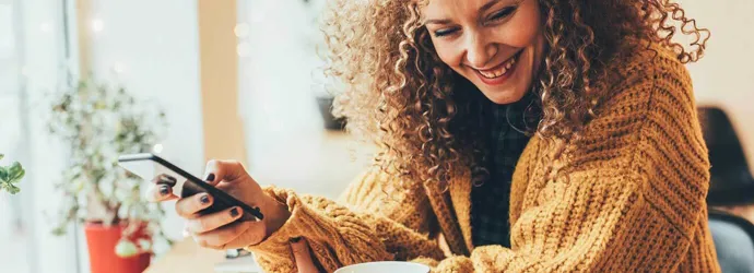 a lady with curly hair smiling at her mobile phone