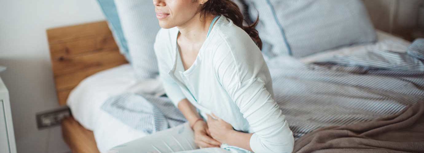 Woman sitting on her bed with abdominal pain