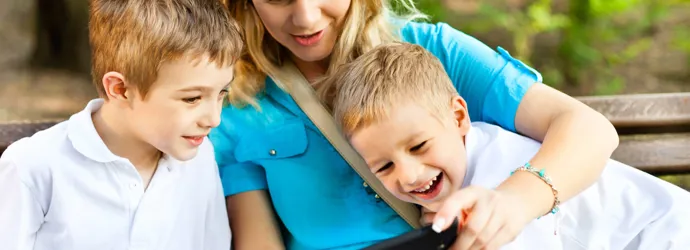 A woman sitting in the middle of two young boys showing them something on her phone