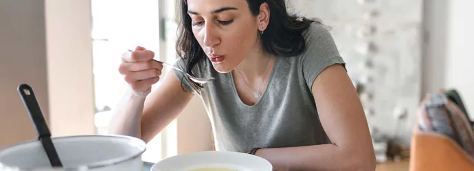 Woman with dark hair eating broth at home as a remedy for watery eyes with a cold