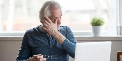 Elderly man in front of a laptop itching one eye