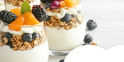 Layered yogurt parfaits topped with granola and fresh fruit such as blueberries, blackberries and orange segments.