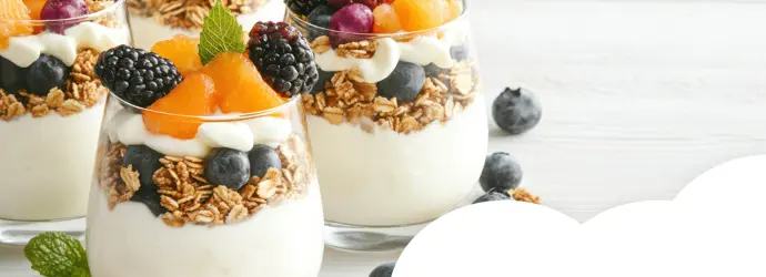 Layered yogurt parfaits topped with granola and fresh fruit such as blueberries, blackberries and orange segments.