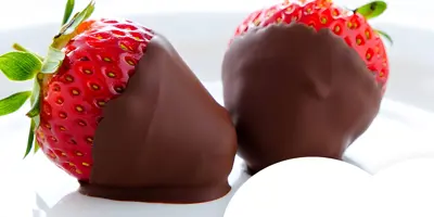 Close-up of two strawberries partially dipped in chocolate, served on a white plate.