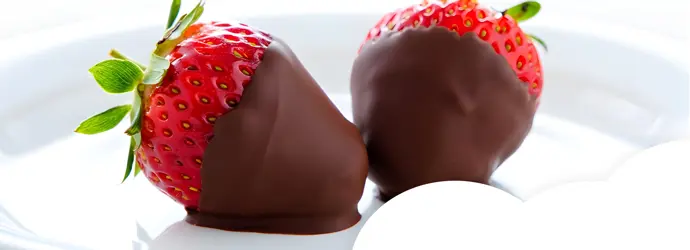 Close-up of two strawberries partially dipped in chocolate, served on a white plate.